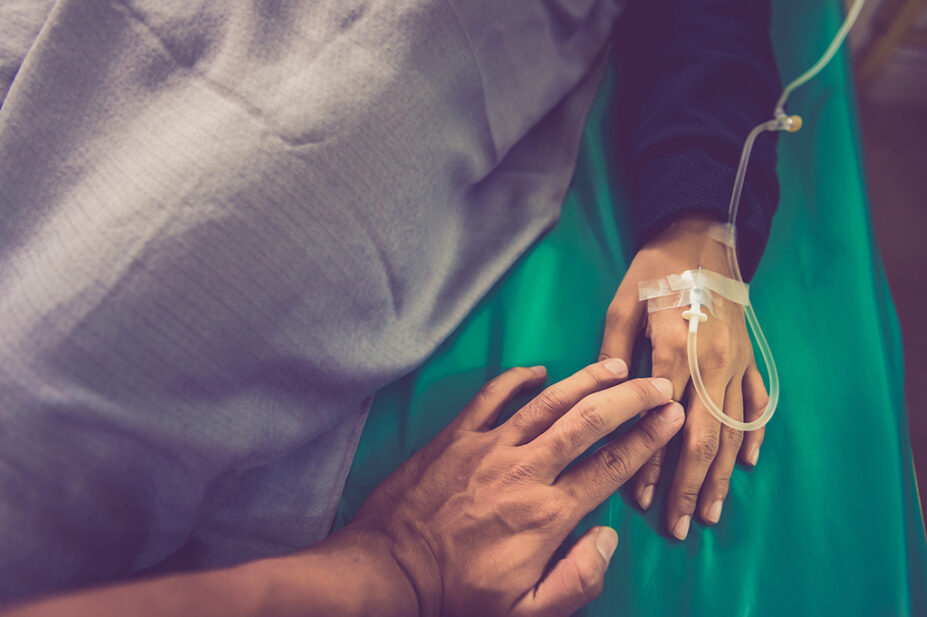 Someone holding older person's hands in sick bed