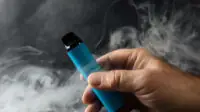 Man holds vape after exhaling its smoke