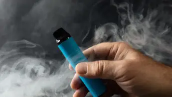 Man holds vape after exhaling its smoke