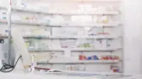 A pharmacy counter with stock shelves of medicines in the background