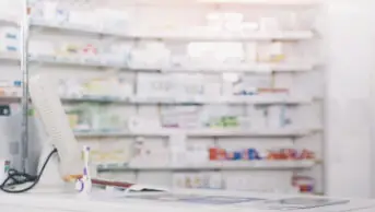 A pharmacy counter with stock shelves of medicines in the background