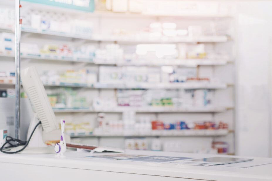 A pharmacy counter with stock shelves of medicines in the background