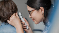 A GP examining boy's ear with otoscope