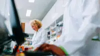 Pharmacists working behind a counter, one with a computer