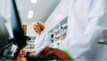 Pharmacists working behind a counter, one with a computer