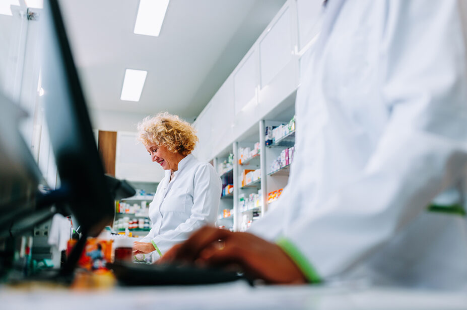 Pharmacists working behind a counter, one with a computer