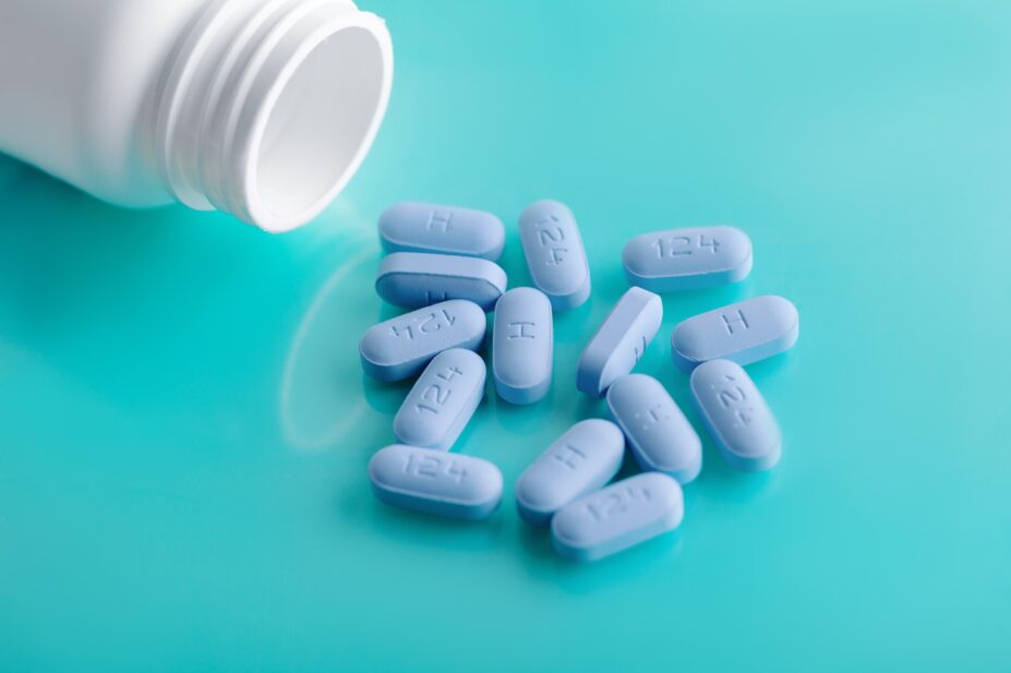 Photo of an open bottle of prescription PrEP Pills spilling out onto a reflective blue table