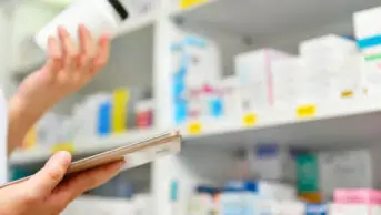 Pharmacist holds medicine bottle and computer tablet