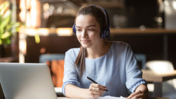 A woman taking notes while using a laptop