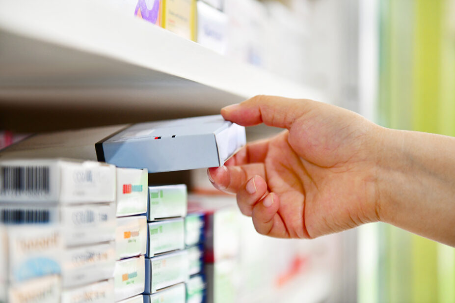 Close up of pharmacist's hand taking box of medicines off a shelf