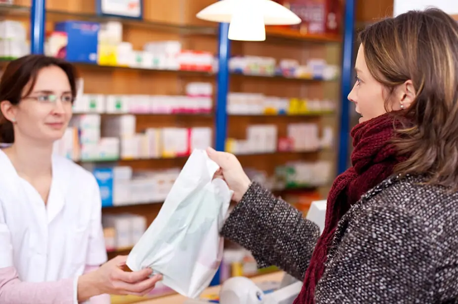 Pharmacy employee passes customer a prescription bag