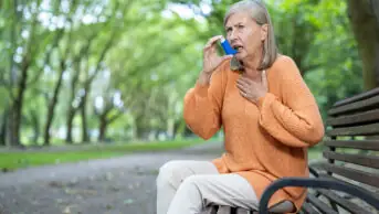 An older woman uses an inhaler while outdoors