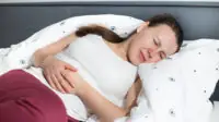 A woman lying on a bed with cramping symptoms of Crohn's disease