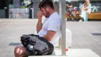 Man sits on a plinth in central London visibly very hot, during a heatwave
