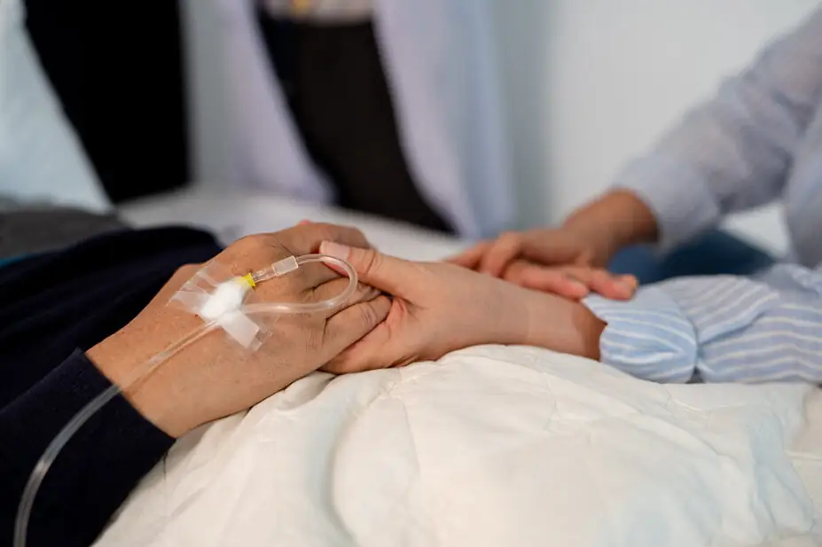 Bedridden patient holding someone's hand