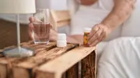 An elderly man laying in bed prepares to take medication with a glass of water