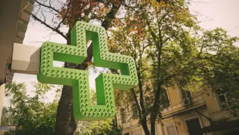 A green medical cross sign outside of a community pharmacy