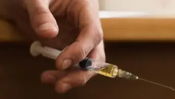 Hand holding injectable drug, suggesting drug addiction and misuse