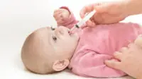 A newborn baby receives medicine in its mouth via syringe