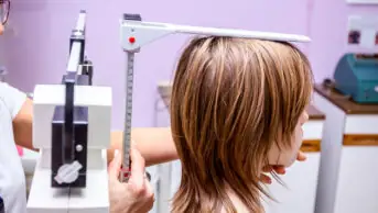 Preschooler is having systematic examination, standing on scale for measuring weight and height in doctor's office.