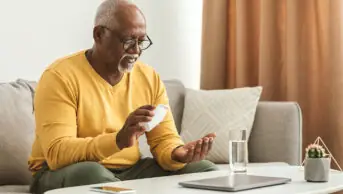 An older man takes medicine with a glass of water