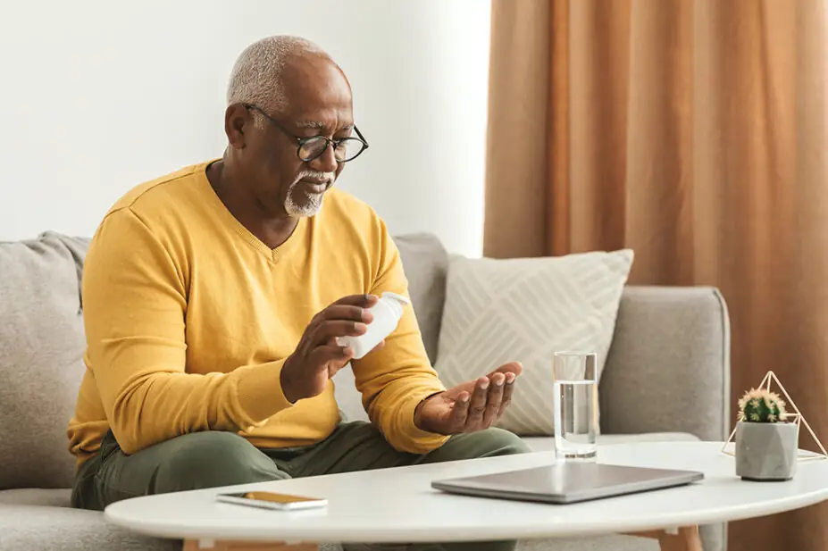 An older man takes medicine with a glass of water