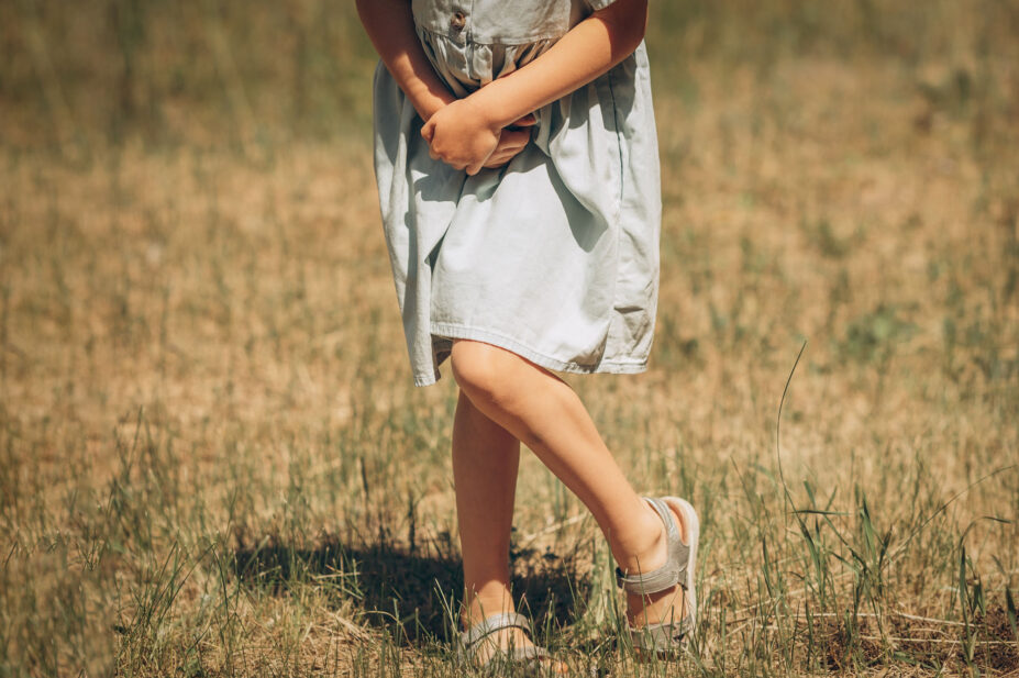 Young girl with clasped hands, in discomfort in a field