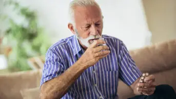 An older man takes his medication with a glass of water