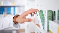 A pharmacist reaches for a prescription on a shelf