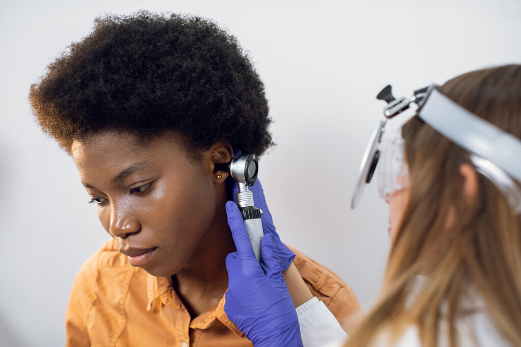 Ear exam. Close up of female young doctor looking at a patient's ear with otoscope
