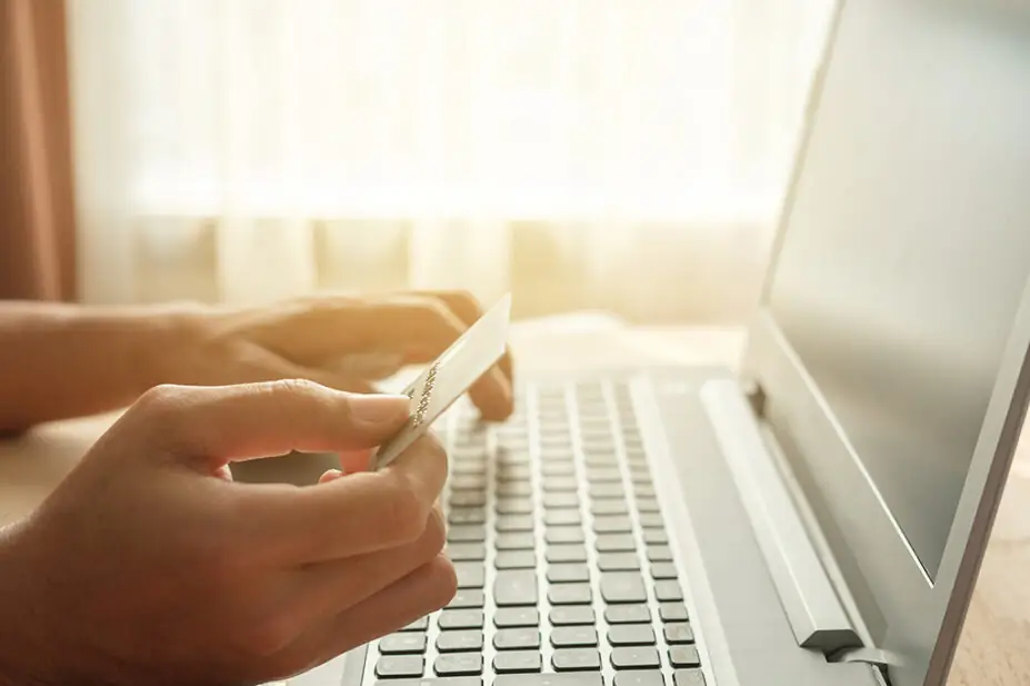 Someone buying something on their laptop with a debit or credit card in their hand