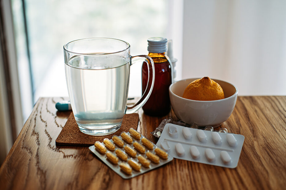 A table containing a cup of water, medicines and an orange