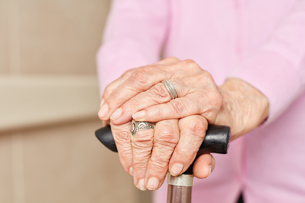 A close-up of an older woman's hands holding a cane