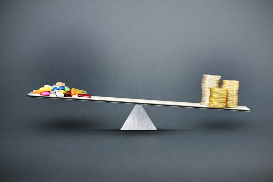 Concept of spending money on medicines and drugs with metallic scale with pills and pile of money on dark background