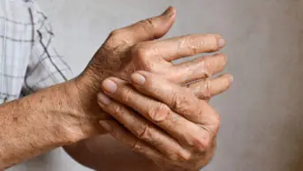 An older man with rheumatoid arthritis massages his hand
