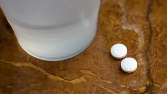 Two tablets of aspirin next to a glass of water