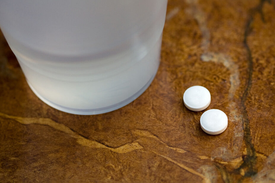 Two tablets of aspirin next to a glass of water