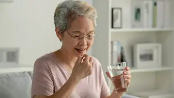 An older woman takes medication with a glass of water