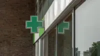 A green cross sign outside of a community pharmacy