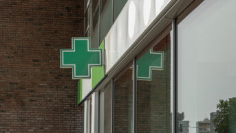 A green cross sign outside of a community pharmacy