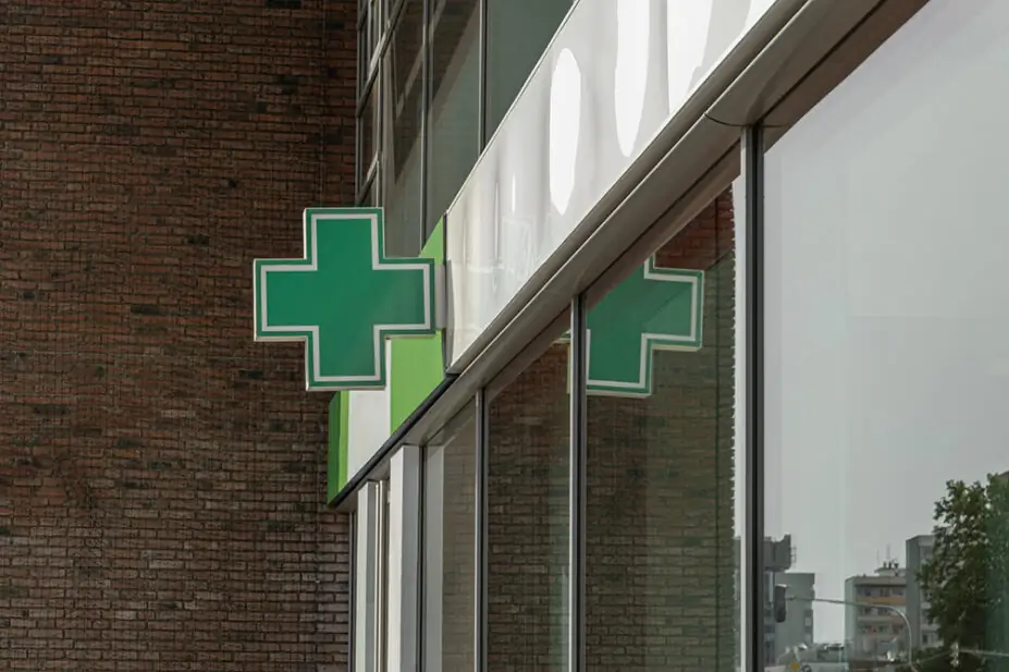 A green cross sign outside of a community pharmacy