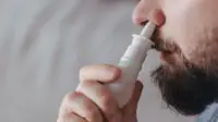 A man uses a nasal decongestant spray