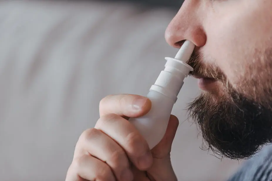 A man uses a nasal decongestant spray