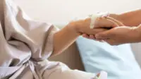 A close-up of a person holding an older patient's hand with an IV