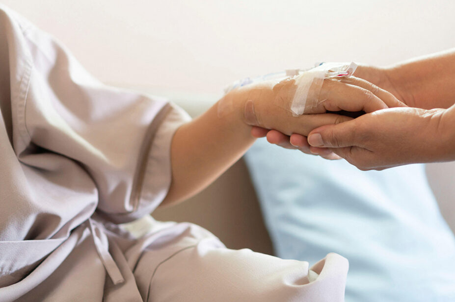 A close-up of a person holding an older patient's hand with an IV