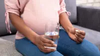 A pregnant woman takes a tablet with a glass of water