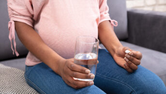 A pregnant woman takes a tablet with a glass of water