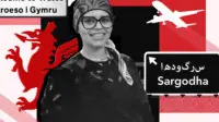 Rafia Jamil stands in front of a red and black backdrop, she wears glasses, headscarf and black top. She smiles. In the background is a sign for Wales, a Welsh dragon in red, a street sign for Sargodha and a silhouette of a plane