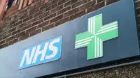 NHS pharmacy sign with green cross on brick wall