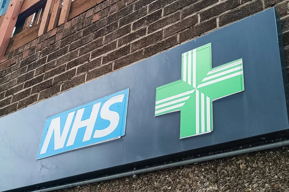 NHS pharmacy sign with green cross on brick wall